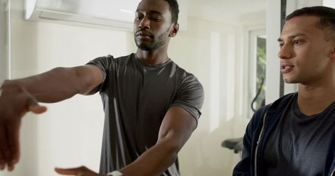 Black personal trainer demonstrating arm extension to south asian client in home gym