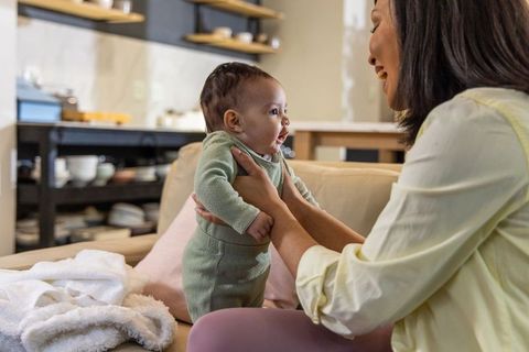 Smiling mother holding baby on sofa at home, joyful bonding and cozy family moment