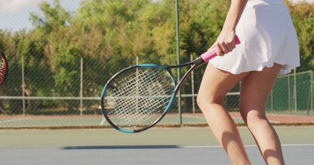 Female tennis player holding racket during a match on an outdoor court. Ideal for promoting sports activities, healthy lifestyle, exercise routines, and women's fitness.