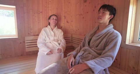 Sunlit sauna relaxation with asian man and african american woman wearing bathrobes