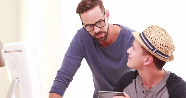 A young Caucasian man is mentoring a teenage boy on a computer task, with copy space - Download Free Stock Photos Pikwizard.com