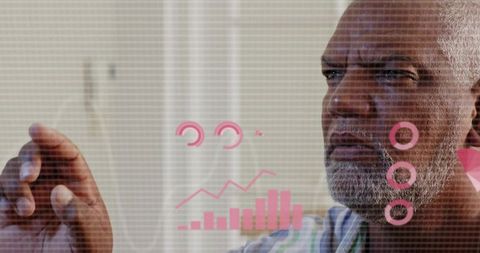 Senior man manipulating holographic analytics dashboard with pink charts in home office