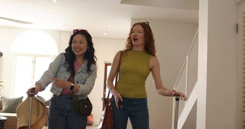 Friends arriving with luggage and straw hat in bright modern home foyer