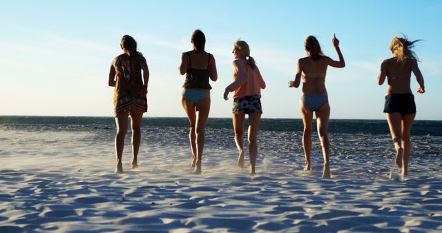 Group of friends running on a sandy beach during sunset. Ideal for themes of friendship, fun, summer vacations, outdoor activities, and carefree lifestyle.