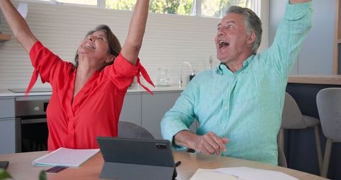 Senior Couple Celebrating with Digital Tablet and Documents Overwhelmed with Joy