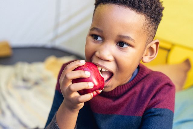 Happy african american boy eating red apple in sitting room - Download Free Stock Photos Pikwizard.com