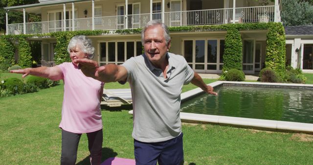 Happy caucasian senior couple practicing yoga in garden standing and stretching in the sun. at home in isolation during quarantine lockdown.