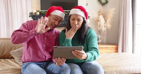 Joyful senior couple video calling during holidays with santa hats