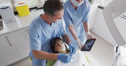 Dentists Reviewing Dental X-Ray on Tablet While Examining Patient in Clinic