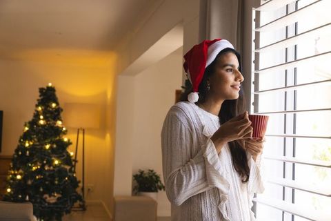 Woman in Santa Hat Holding Mug by Window During Festive Season