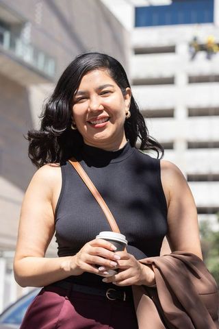 Smiling professional woman holding coffee on sunlit city street with chic outfit