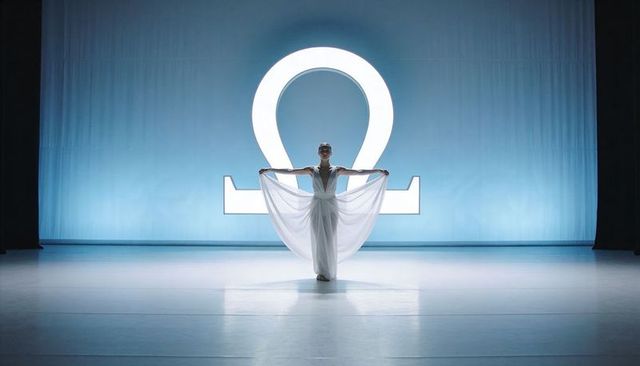 Dancer Holding Flowing Gown on Blue-Lit Stage Performing Before Illuminated Omega Loop