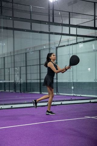 Indian woman balancing on one leg while playing padel on vibrant purple court