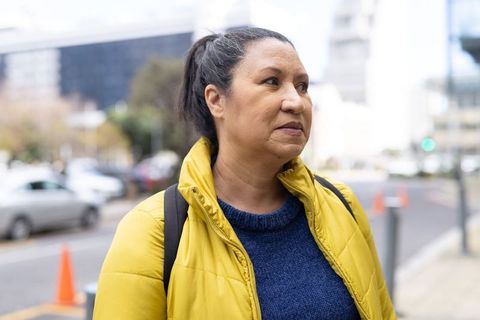 Contemplating urban commuter wearing yellow puffer jacket and navy sweater with backpack