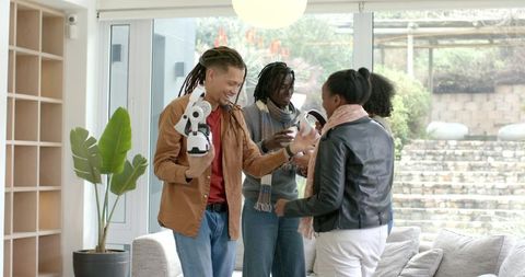 Multiracial friends testing home robot and headset, sharing tech joy in modern living room