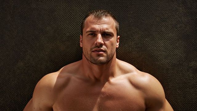 Muscular shirtless man showcasing defined chest and shoulders on dark textured backdrop