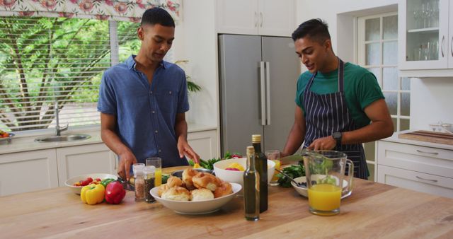 Two friends are preparing a healthy meal together in a bright and modern kitchen. They are chopping vegetables and fruits, and a variety of fresh ingredients are spread across the countertop, including bell peppers and croissants. This image is perfect for promoting healthy living, cooking tutorials, diet blogs, and friendship or teamwork concepts.