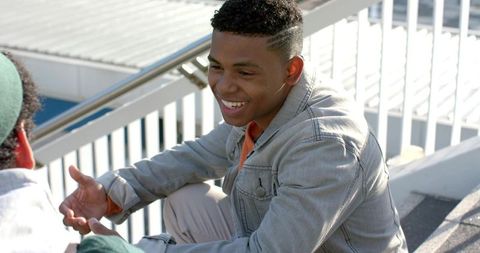 Sunlit african american friends chatting on rooftop steps, casual denim jacket and smiling