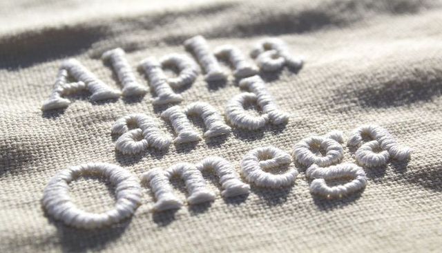 Raised white alpha omega embroidery on beige woven textile macro detail for branding