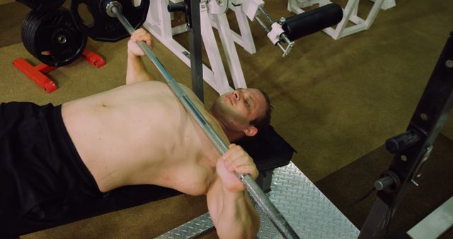 This image depicts a man weightlifting on a bench in a gym, likely working on building upper body strength. This could be used in fitness and workout promotions, gym advertisements, or motivational fitness blogs.
