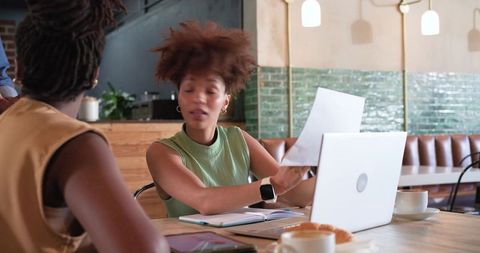 Young professional presenting paperwork during cafe coworking meeting with laptop and coffee