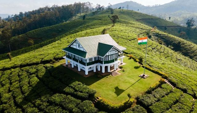 Colonial bungalow overlooking lush tea plantation with indian tricolor on hillside