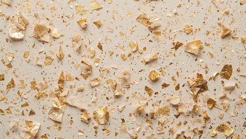 Gold foil flakes and torn beige paper fragments on neutral background for luxury texture