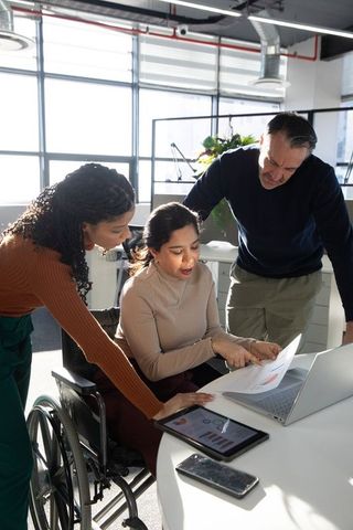 Inclusive business team collaborating on charts and tablet at sunlit modern office table