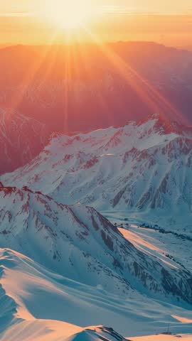 Gliding camera capturing snowy alpine peaks at sunrise with golden sun rays vertical video