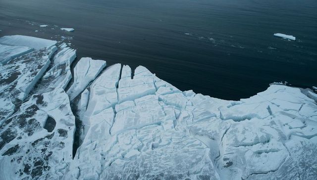 Aerial view of fractured polar ice shelf meeting dark open ocean with calving crevasses