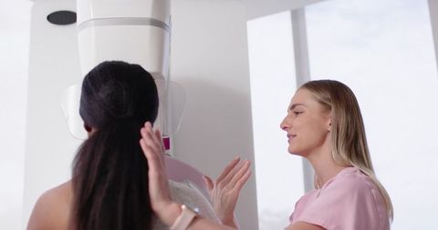 Mammography technologist guiding patient during breast screening with digital gantry