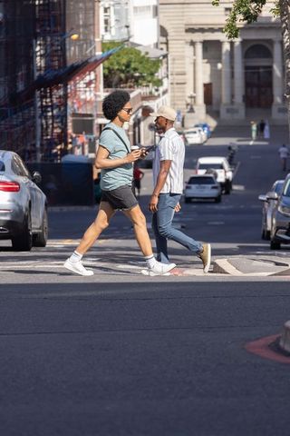 Two african american men crossing hilly city street with coffee and smartphone
