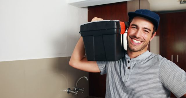 Smiling handyman carrying a toolbox in a modern kitchen. Ideal for advertisements, brochures, and websites related to home maintenance, repair services, plumbing, or professional handyman services.
