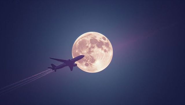 Airplane silhouette against full moon at night