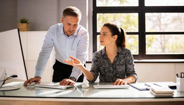 Business team reviewing project on desktop with manager leaning in and colleague explaining