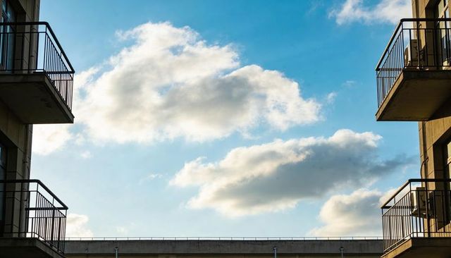 Framing blue sky through urban balcony gap with cumulus clouds and metal railings