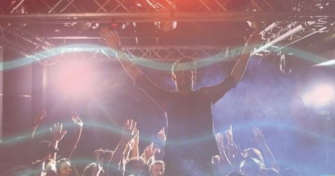 Energetic concert crowd cheering while man raises arms under stage lights, fog and phones
