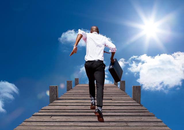 Businessman running upwards on a wooden boardwalk with a blue and cloudy sky background while holding a briefcase. Suitable for illustrating business ambition, career progression, growth, leadership, success, and motivational concepts.