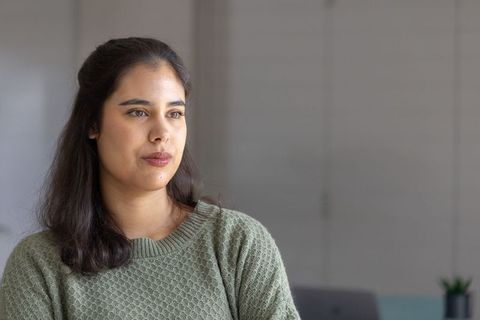 Contemplative indian woman in green knit sweater seated indoors in soft natural light