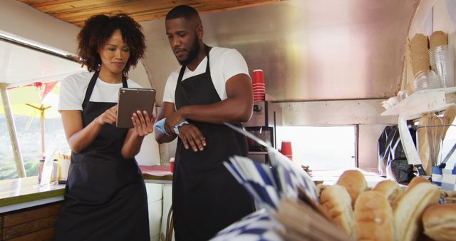 African american couple wearing aprons smiling while using digital tablet in the food truck. food truck and street food concept