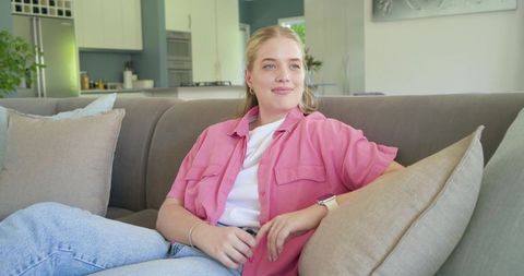 Young woman relaxing on modern sofa wearing pink overshirt and smartwatch, casual home