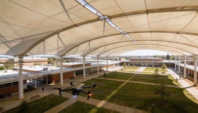Drone capturing aerial view of university courtyard under curved tensile canopy