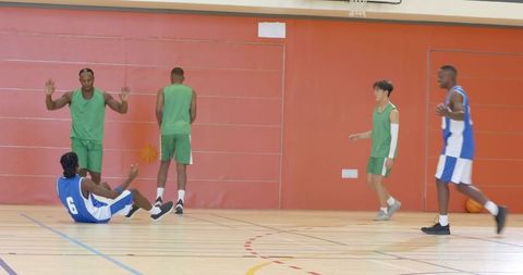 Basketball player falling after crossover, teammate offering hand, players regrouping on court