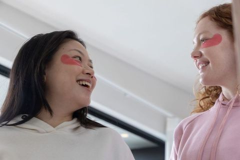 Teen friends laughing with heart under-eye patches wearing hoodies casual friendship portrait