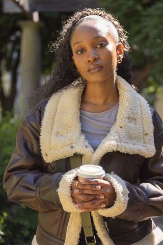 African woman holding takeaway coffee wearing shearling jacket making eye contact
