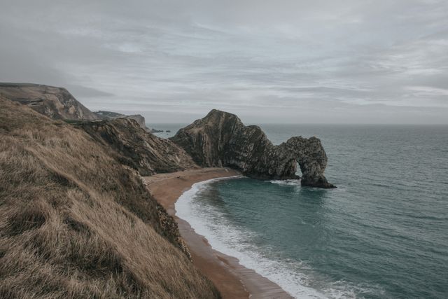 Durdle Door on the Jurassic Coast in Dorset, England showcases an iconic rock arch. This serene and overcast coastal scene is ideal for travel promotions, nature photography collections, landscape decorating ideas, and educational materials highlighting geological formations.