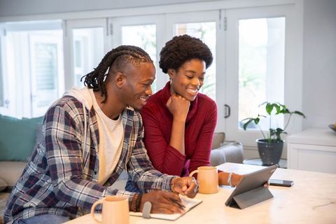 Smiling Couple Collaborating at Home with Digital Tablet and Notebook