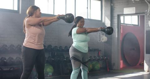Diverse women swinging kettlebells in bright gym for strength and functional fitness