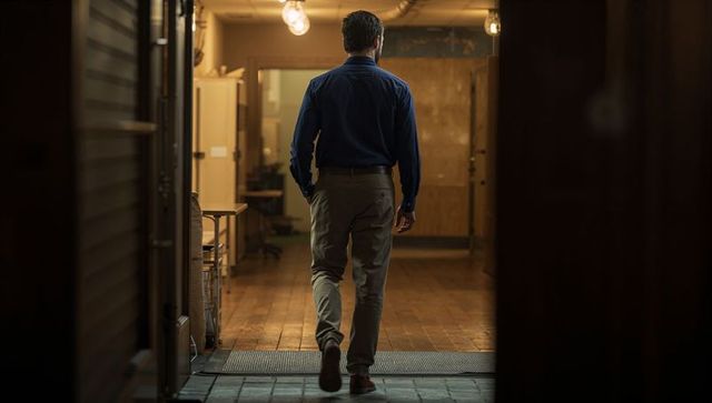Man walking in dark blue shirt and khaki trousers down dim industrial workshop corridor