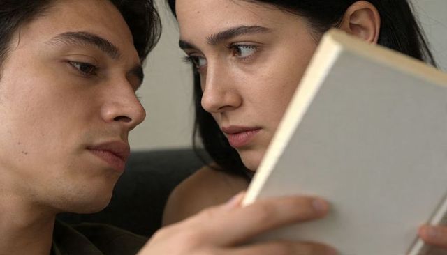 Intimate close-up of young couple reading together on sofa, focused hands holding book